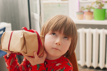 Caucasian boy in red pijamas crafing decorations or opening presents  at home candid shot
