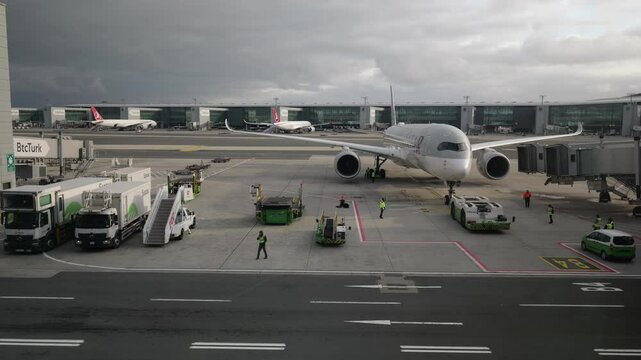 Istanbul, Turkey - 12 1 2024: Pushback truck pushing Qatar Airways Airbus 350 aircraft backward departing from airport terminal gate with loading bridge detached and ground operators at work on tarmac