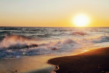 Sunrise on sandy beach against the backdrop of stormy waves.