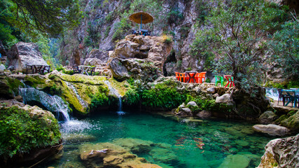 
A natural turquoise pool in Akchour, Chefchaouen, surrounded by lush green rocks. Colorful tables...