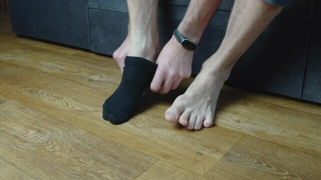 A man puts on old black socks, one of which has a hole in the big toe