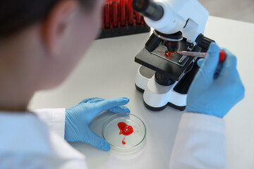 Laboratory testing. Doctor dripping blood sample onto glass slide while working with microscope at...