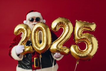 A Santa Claus holding golden foil balloons in the shape of the numbers "2025", isolated on red background.