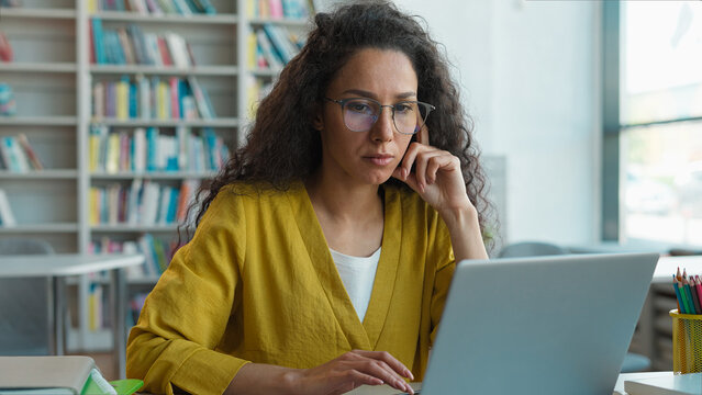 Latina Caucasian Hispanic woman working typing laptop desktop computer pc library university research project educate technology e-learning student diploma contemplation aspirations girl female study