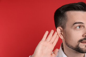 Man showing hand to ear gesture on red background, closeup. Space for text