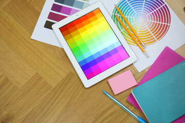 Designer's workplace with tablet, palettes and stationery on wooden table, flat lay