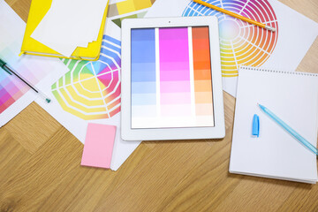 Designer's workplace with tablet, palettes and stationery on wooden table, flat lay