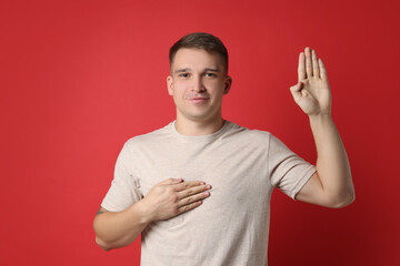 Man making promise with raised hand on red background. Oath gesture