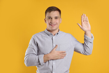 Man making promise with raised hand on orange background. Oath gesture