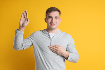 Man making promise with raised hand on orange background. Oath gesture