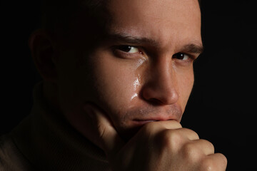 Distressed young man crying on black background, closeup