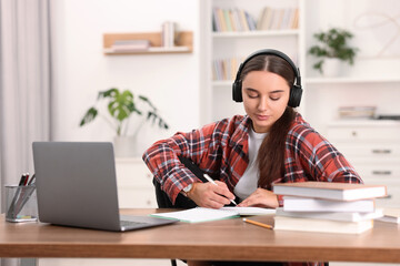 Student in headphones studying at wooden table indoors
