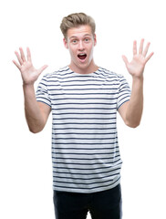 Naklejka premium Young handsome blond man wearing stripes sailor t-shirt very happy and excited, winner expression celebrating victory screaming with big smile and raised hands