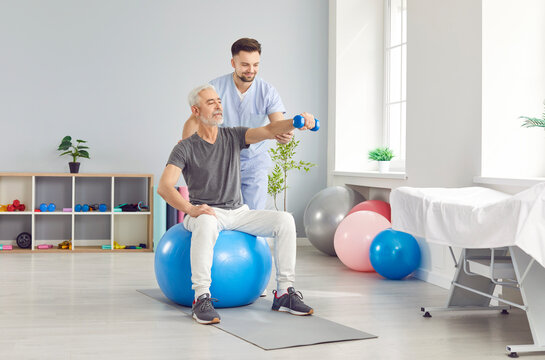 Senior man health care rehabilitation with ball, dumbbells and physical therapist, nurse or sport instructor doing exercise to help elderly in active aging, adapted sport activity for older people