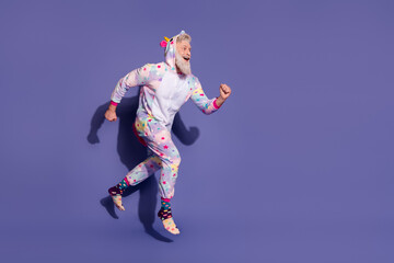 Joyful man in colorful unicorn costume against vibrant purple backdrop running enthusiastically