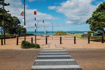 Peaceful coastal scene. People relax near a modern art piece overlooking the ocean. Sunny day at Moana Reserve. , OREWA, AUCKLAND, NEW ZEALAND