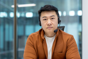 Asian man working in an office while using a headset for communication and teamwork.