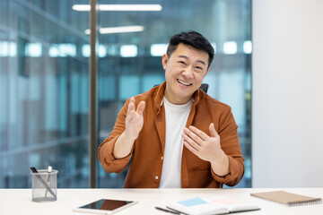 Fototapeta premium Asian man expressing ideas while seated at a desk in an office setting, conveying confidence, positivity, and communication during a business-related discussion or meeting.