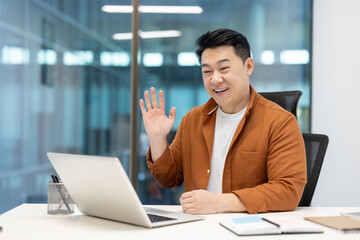 Asian man in a professional setting, engaging in an online video call at work.