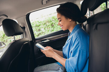 Young woman enjoying a car ride while texting on her phone during a sunny day in the city, reflecting relaxation and casual style.
