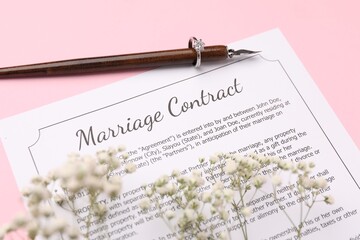 Marriage contract, flowers, pen and ring on pink background, above view