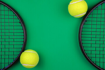 Two lawn tennis rackets lie opposite each other on the sides on a green background with a place for text, next to them are yellow tennis balls with a white stripe. The concept of sports and games