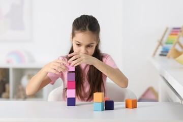Fototapeta premium Girl building tower of colorful cubes at table indoors