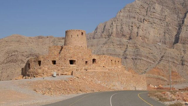 historic stone fort in Bukha, Musandam, Oman, against the backdrop of mountains, with the Omani flag waving from the tower Al Qalaa Fort