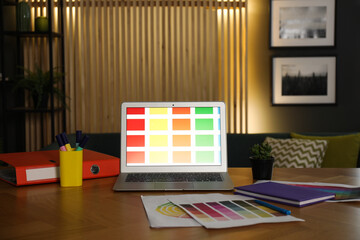 Designer's workplace with laptop, stationery and palettes on wooden table indoors