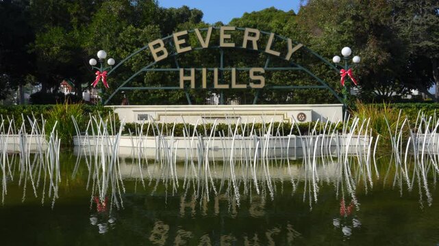 Beverly Hills, California - December 6, 2024: Iconic Beverly Hills sign adorned with festive decorations, surrounded by greenery and reflective water.