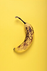 Single overripe banana top view on yellow background with copy space