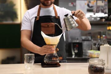 Barista brewing coffee in glass coffeemaker with paper filter at table in cafe, closeup