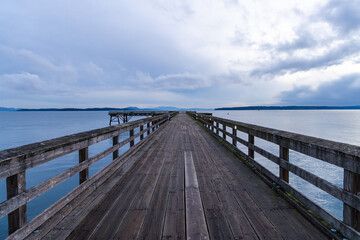Fototapeta premium Peaceful Wooden Pier Extending Over Calm Ocean Waters at Sunset