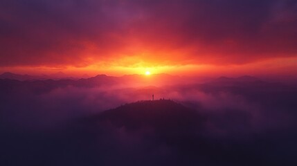 Vibrant sunset over misty mountains, silhouetted hilltop.
