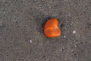 A small orange rock is laying on the sand