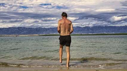man enters the water 
beautiful mountains in the distance 
