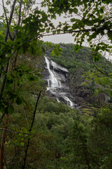 Obraz premium A stunning waterfall flows through a lush forest, tumbling over rocks and surrounded by vibrant greenery. The sound of rushing water blends with the peaceful ambiance, creating a serene natural escape