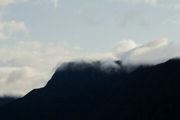 Fototapeta premium Majestic mountains emerge from the mist, their peaks partially shrouded in swirling clouds. The ethereal scene evokes a sense of mystery and grandeur, with nature’s beauty hidden in the fog