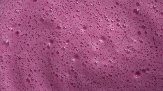 Glass of pink raspberry milkshake, close up, top view. Fresh drink of bright scarlet cranberry or cherry or red viburnum or strawberry. Texture and background of milk smoothie surface with bubbles
