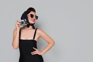 Pin-up woman in sunglasses with camera on grey background, space for text