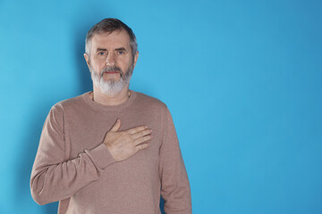 Mature man making promise on light blue background, space for text. Oath gesture