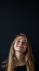 Naklejka premium beautiful young girl smiling looking up on black background with copy space vertically 9:16