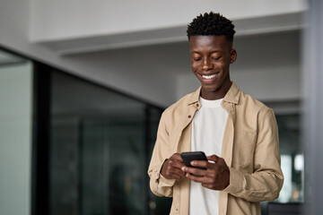 Happy African business man using smartphone standing at work in office. Smiling busy young Black...