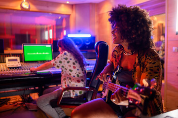Diverse female bass player at recording studio playing guitar.