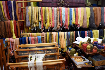 A colorful array of yarns hangs in a traditional textile workshop. Looms, spools, and tools fill the space, showcasing the intricate process of Japanese weaving and natural dyeing crafts.