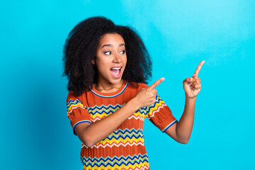 Charming young woman in stylish striped t-shirt pointing with excitement against vibrant blue...