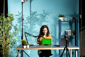 Jolly woman in studio filming chroma key tablet review for tech enthusiasts. Cheerful online star...