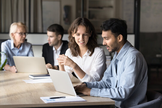 Two multiethnic businesspeople discuss new business platform using laptop, involved in data analysis, reviewing report, or collaborate on project plan, busy in completion work-related task. Teamwork