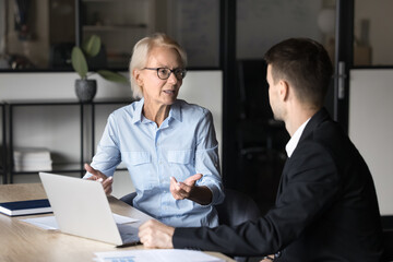 Fototapeta premium Business collaboration, teamwork. Older businesslady provide explanations, share ideas or solution with colleague in office. Manager selling services of company, convince client, conduct negotiations