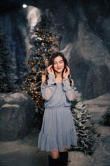 Fototapeta premium Woman smiles in a winter forest with snowfall. Evergreen trees and holiday lights, festive atmosphere for Christmas and New Year celebrations.